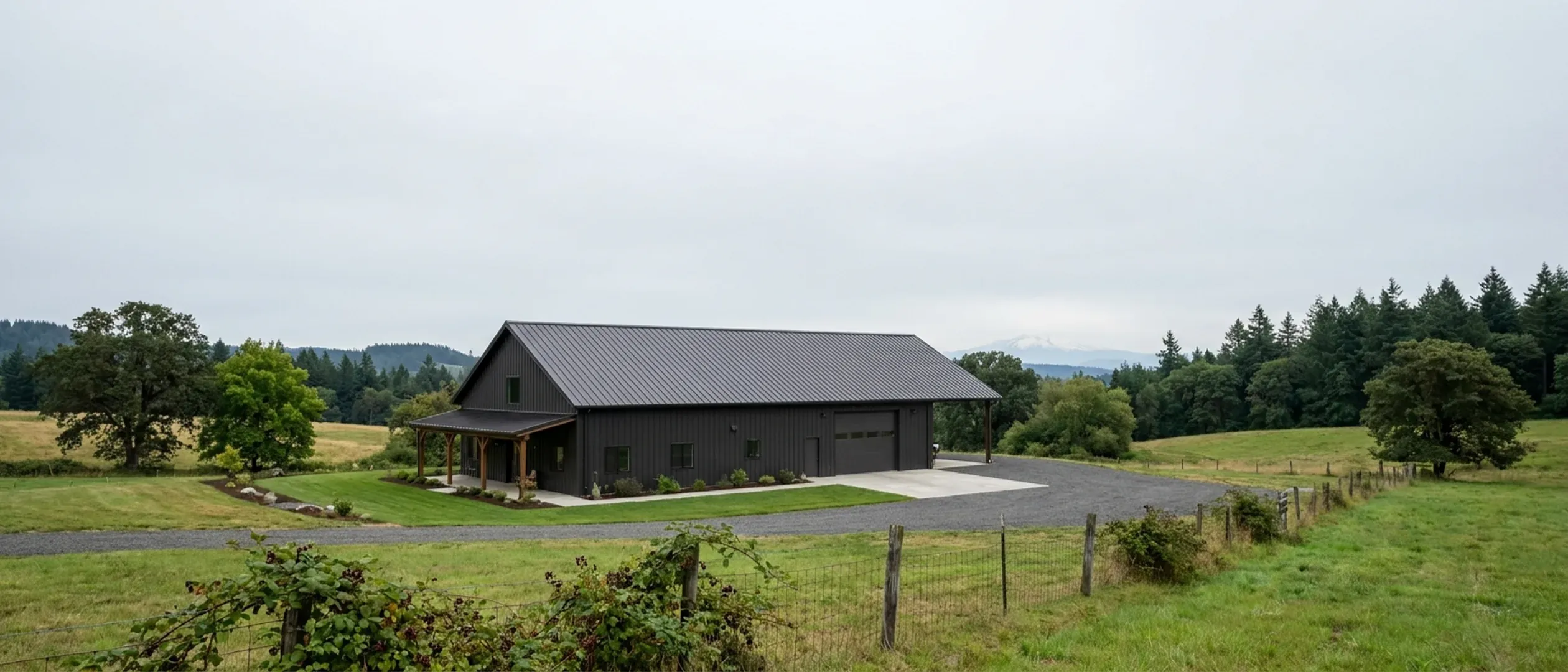 A completed barndominium with a covered entry porch and an attached shop bay, photographed in flat overcast daylight.