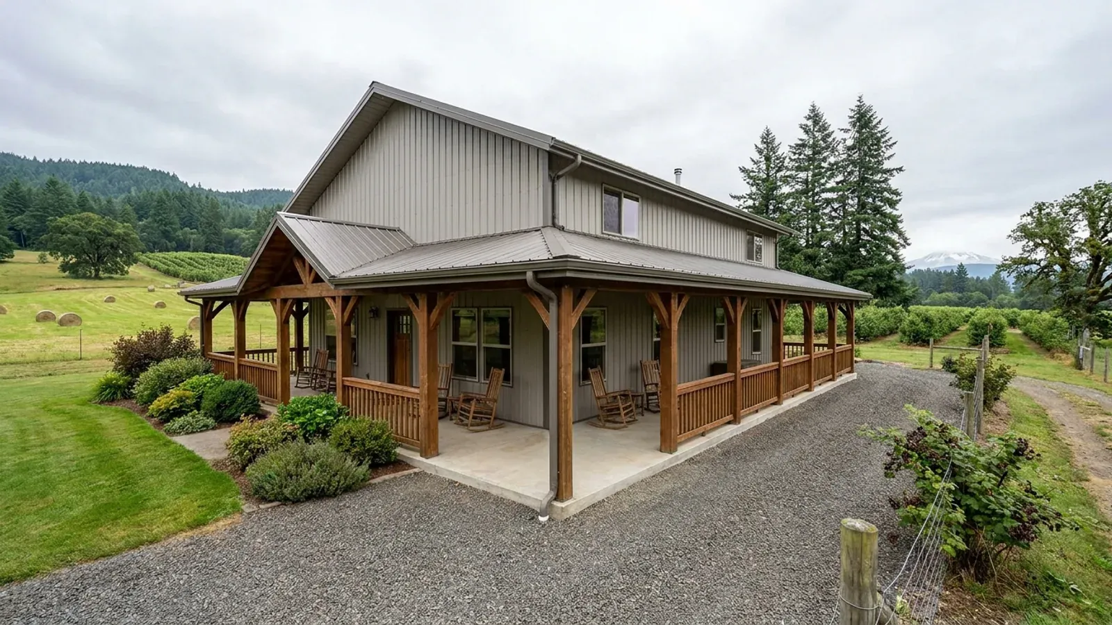 A barndominium exterior showing a deep wrap-around covered porch with posts and railing along two sides of the building.